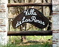 Pilares con pieza de madera irregular con la leyenda: Villa de las Rosas señalizando el acceso